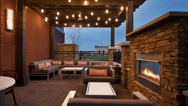 An outdoor patio area with brick flooring, a stone fireplace, and a seating arrangement including sofas and a table.