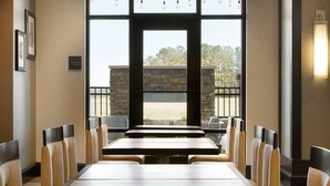 A conference room with a long table and chairs, large windows with a view of the outdoors, and a stone wall.
