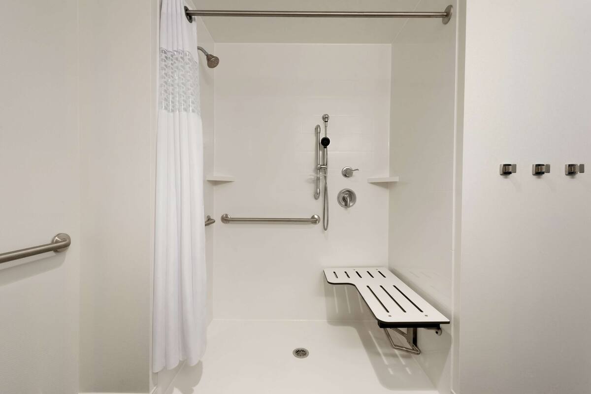 A walk-in shower with a grab bar, a showerhead, and a small bench.