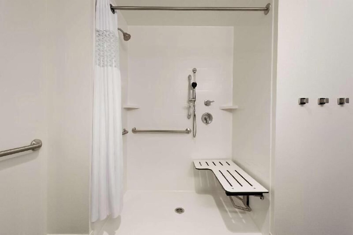 A shower with a grab bar, a showerhead, and a small shelf.