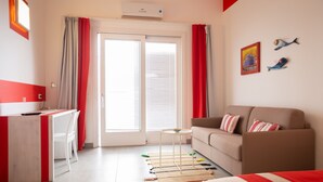 Ein Hotelzimmer mit einem Bett, einem Sofa, einem Schreibtisch mit Stuhl, einem kleinen Tisch und einem Fenster mit Vorhängen.