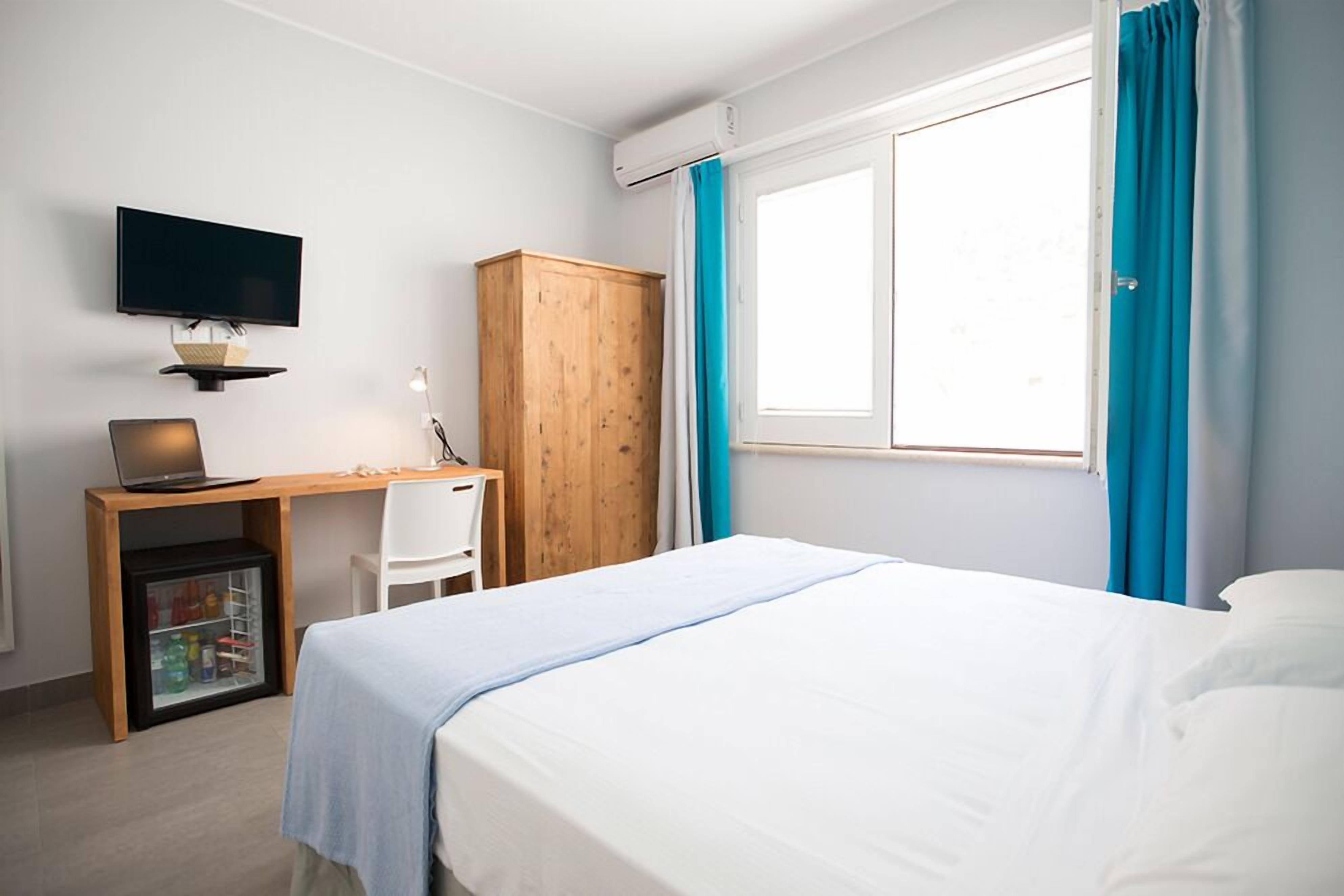 Une chambre d’hôtel comprenant un lit, un bureau avec un ordinateur, une télévision et une armoire.