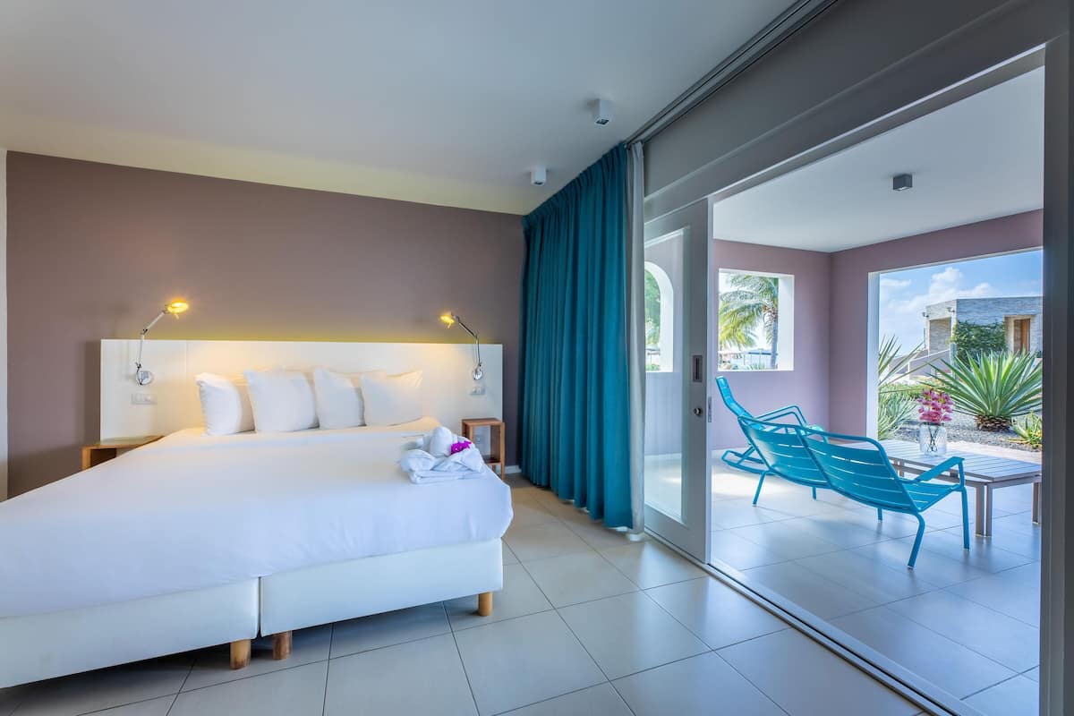 Une chambre d’hôtel dotée d’un grand lit, d’un bureau, d’une chaise et d’une porte-fenêtre coulissante donnant sur un balcon avec une table et des chaises.