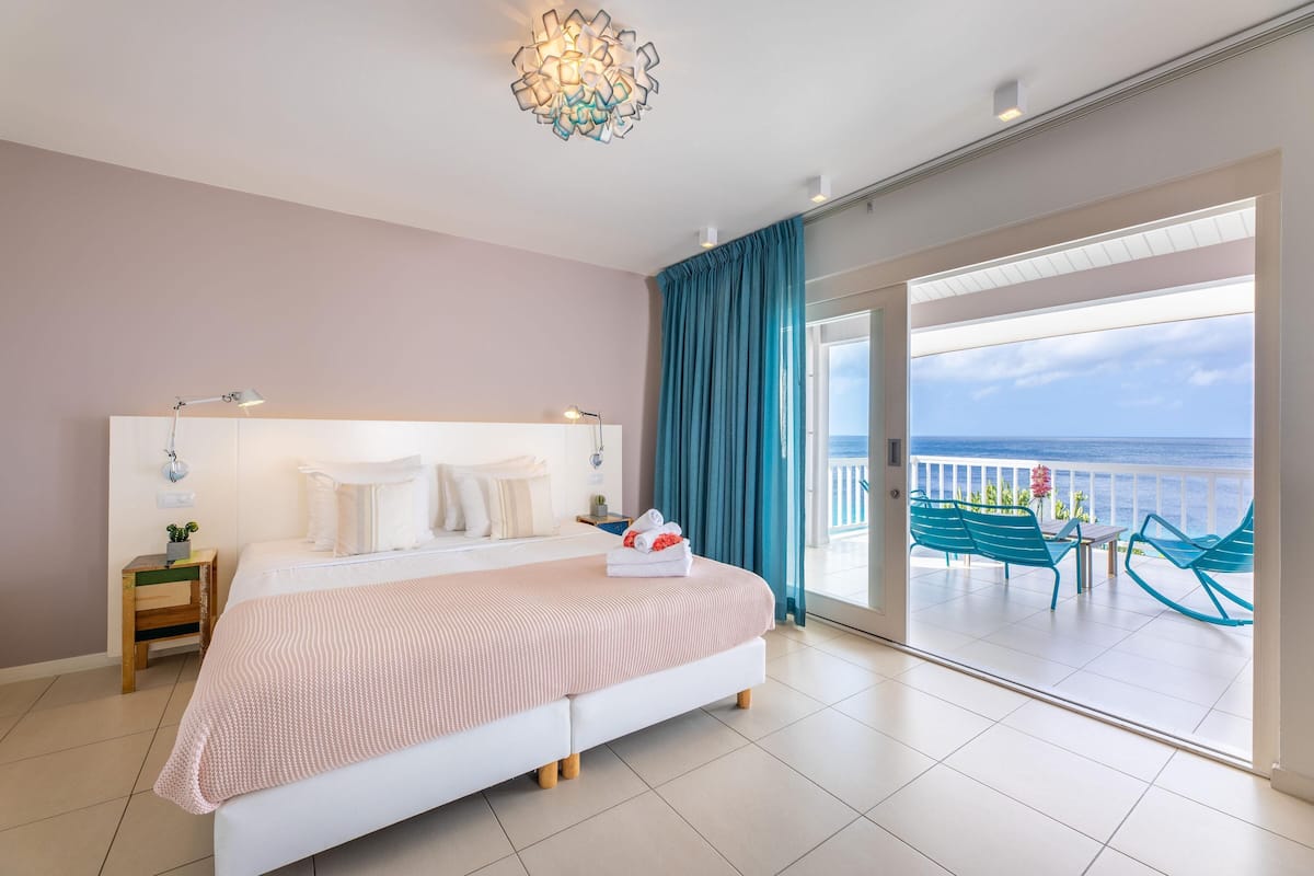 Une chambre à coucher avec un lit, une table de chevet, une lampe et une vue sur la mer depuis un balcon.