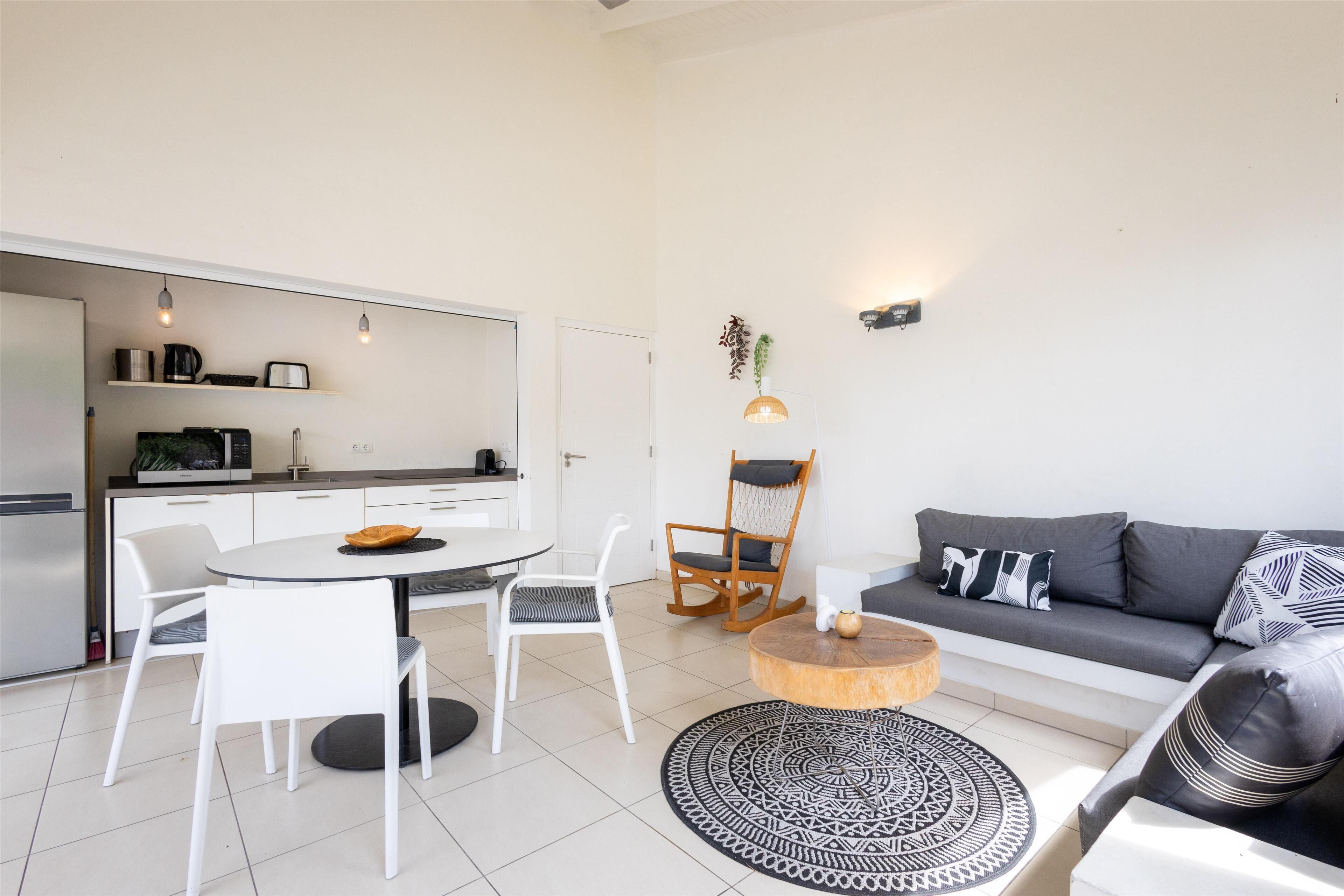 A modern living room with a sofa, a dining table with chairs, a coffee table, and a kitchen area with a refrigerator and cabinets.