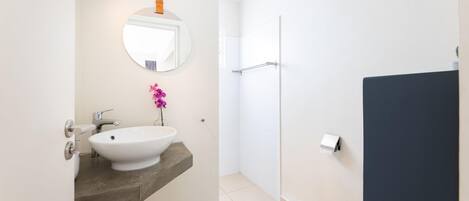 Un baño moderno con un lavabo blanco, un espejo redondo y una zona de ducha.