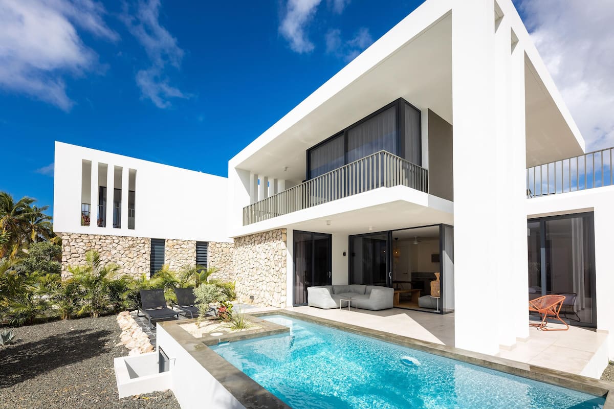Une maison moderne à deux étages, dotée d’une piscine, de murs en pierre et d’un espace de détente extérieur.