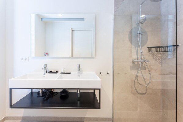 Un baño moderno con un lavamanos blanco, un espejo y una ducha con mampara de vidrio.