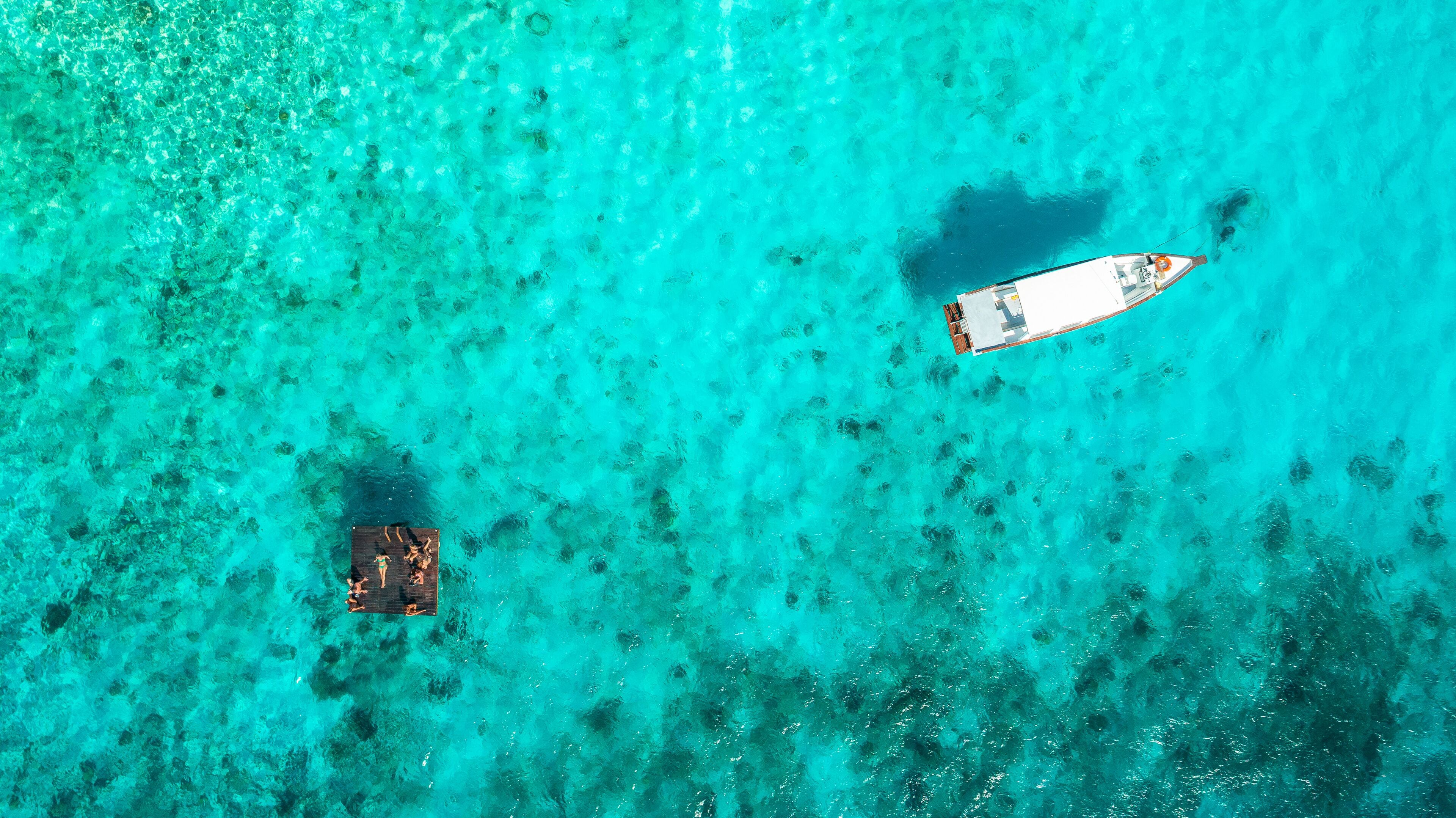 Una vista aerea di un mare turchese con un molo di legno e una barca.
