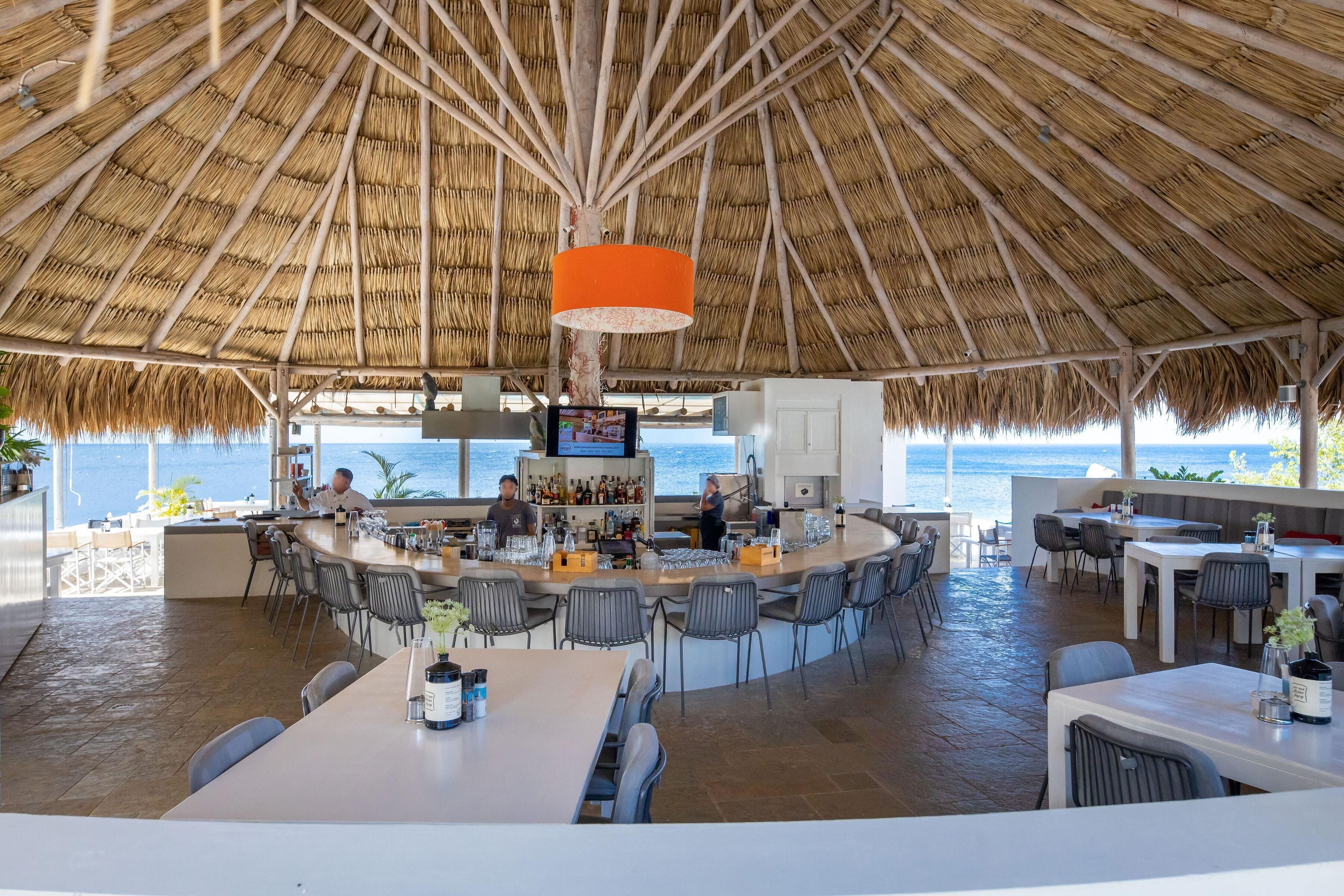 A bar area with a thatched roof, seating, and a view of the sea.