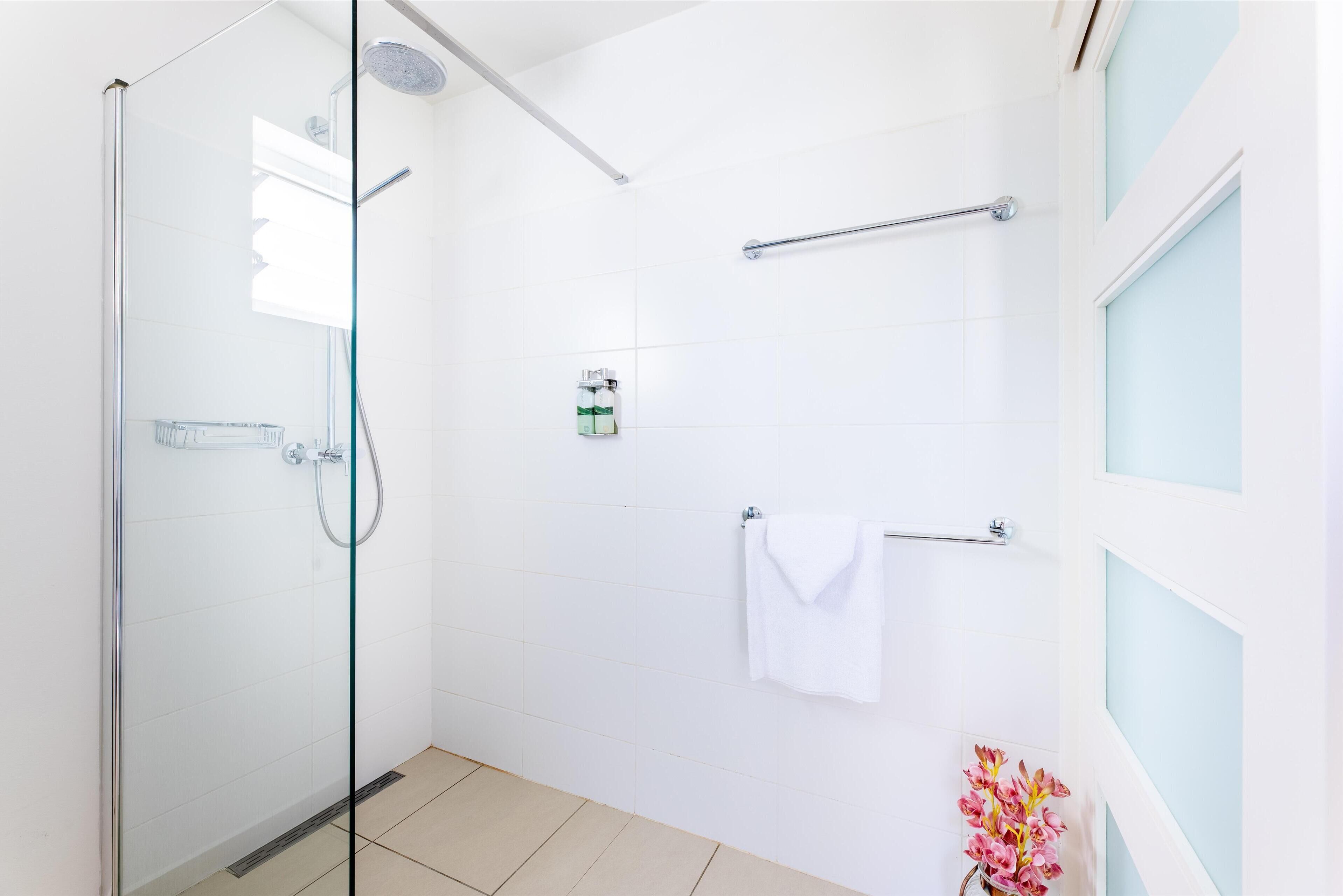 Un bagno moderno con box doccia in vetro, piastrelle bianche, un portasciuga asciugamani e un piccolo ripiano con articoli da toilette.