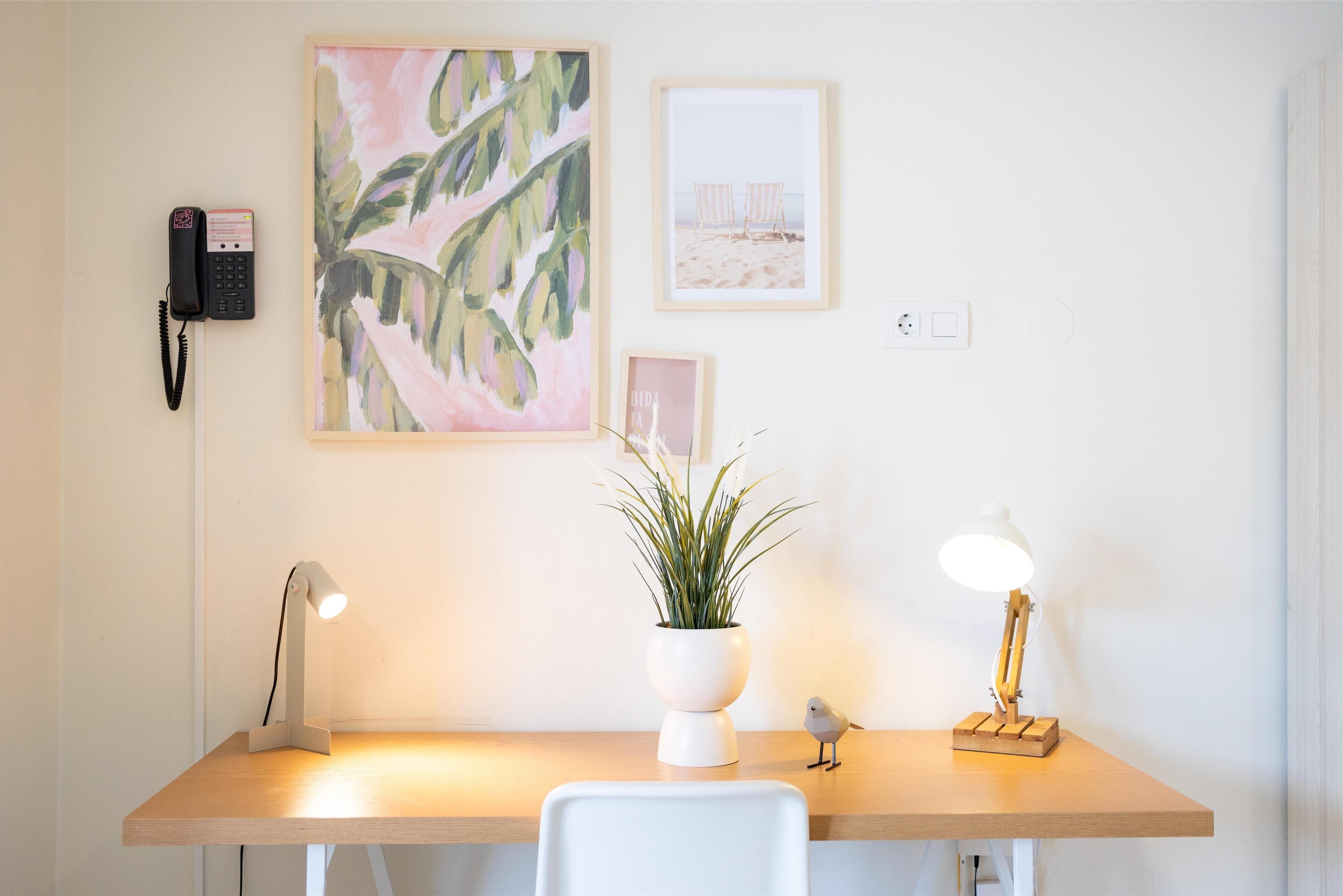 Een bureau met een plant, twee lampen, een telefoon en ingelijste foto's aan de muur.
