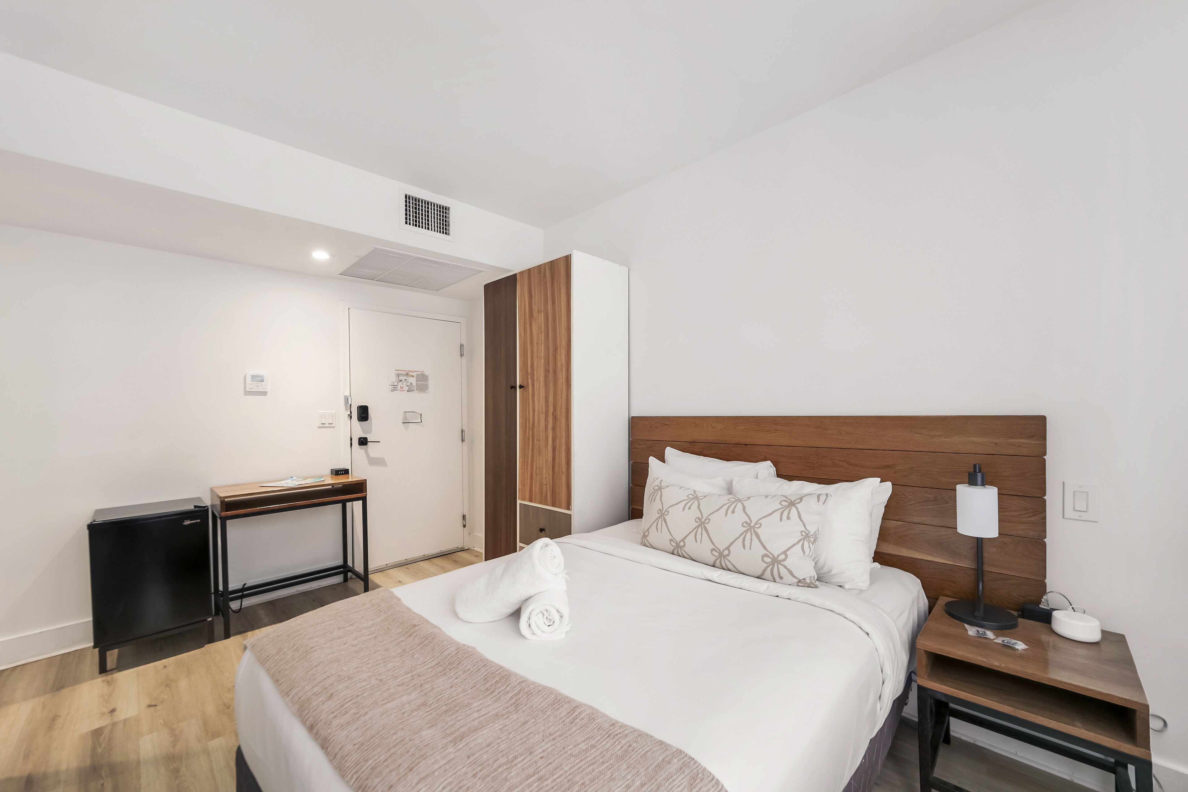 Une chambre d’hôtel comprenant un lit, une table de chevet avec une lampe, un bureau et une armoire.
