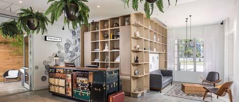 A modern interior with a central wooden desk, shelves with decorative items, and hanging plants.