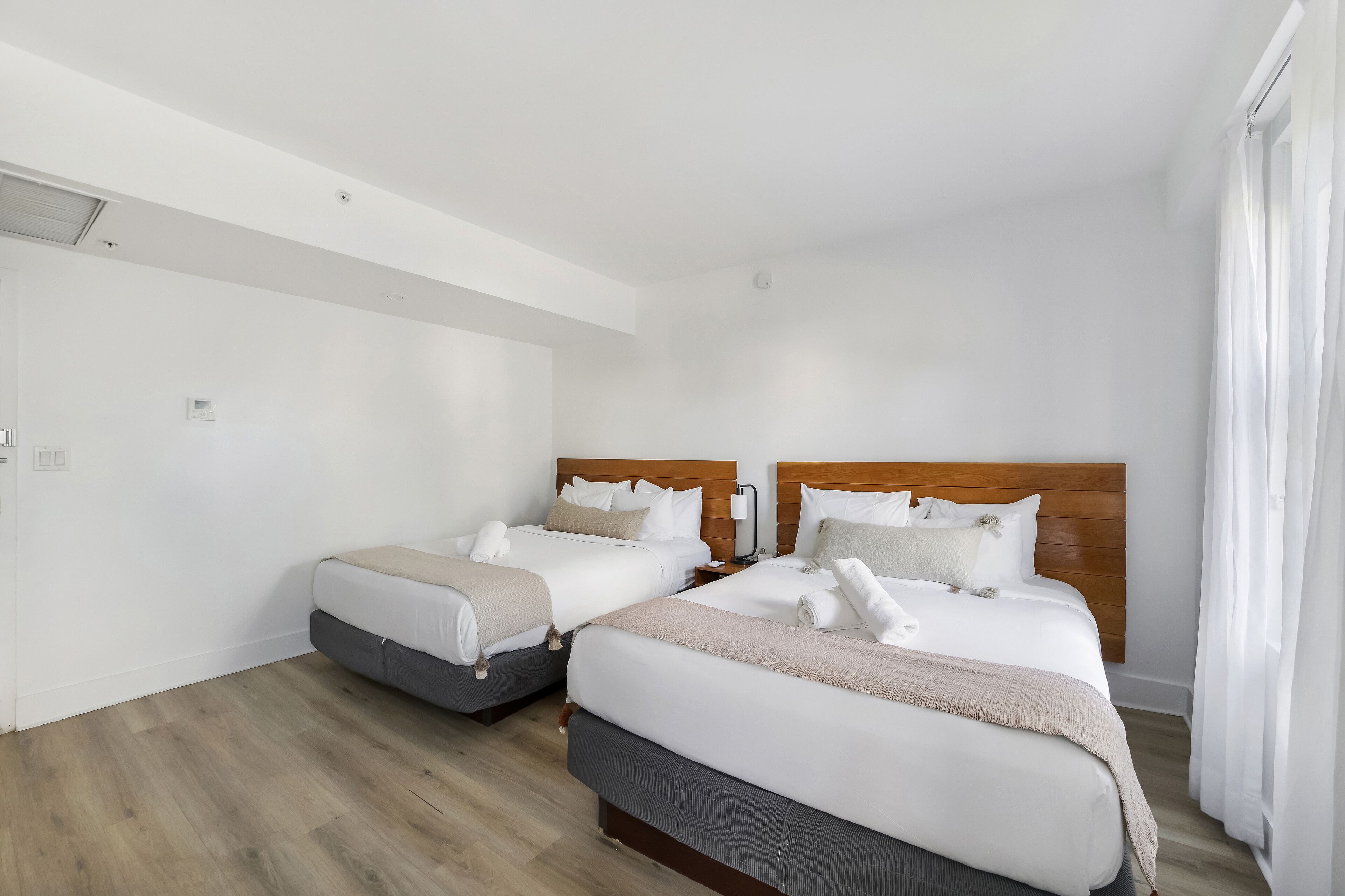 A hotel room with two beds, wooden headboards, white bedding, and a wooden floor.
