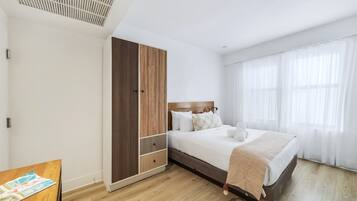 A bedroom with a bed, wooden wardrobe, and a window with sheer curtains.