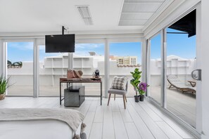 A modern hotel room with a large bed, a desk with a computer, a chair, a TV, and a balcony with a view of buildings. - The Meridian Hotel by At Mine Hospitality (Miami Beach)
