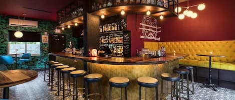 A bar area with a curved counter, multiple stools, a yellow cushioned sofa, and a patterned floor.