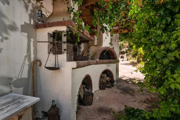 A rustic outdoor area with a brick oven, a hanging lantern, and a wooden bench.