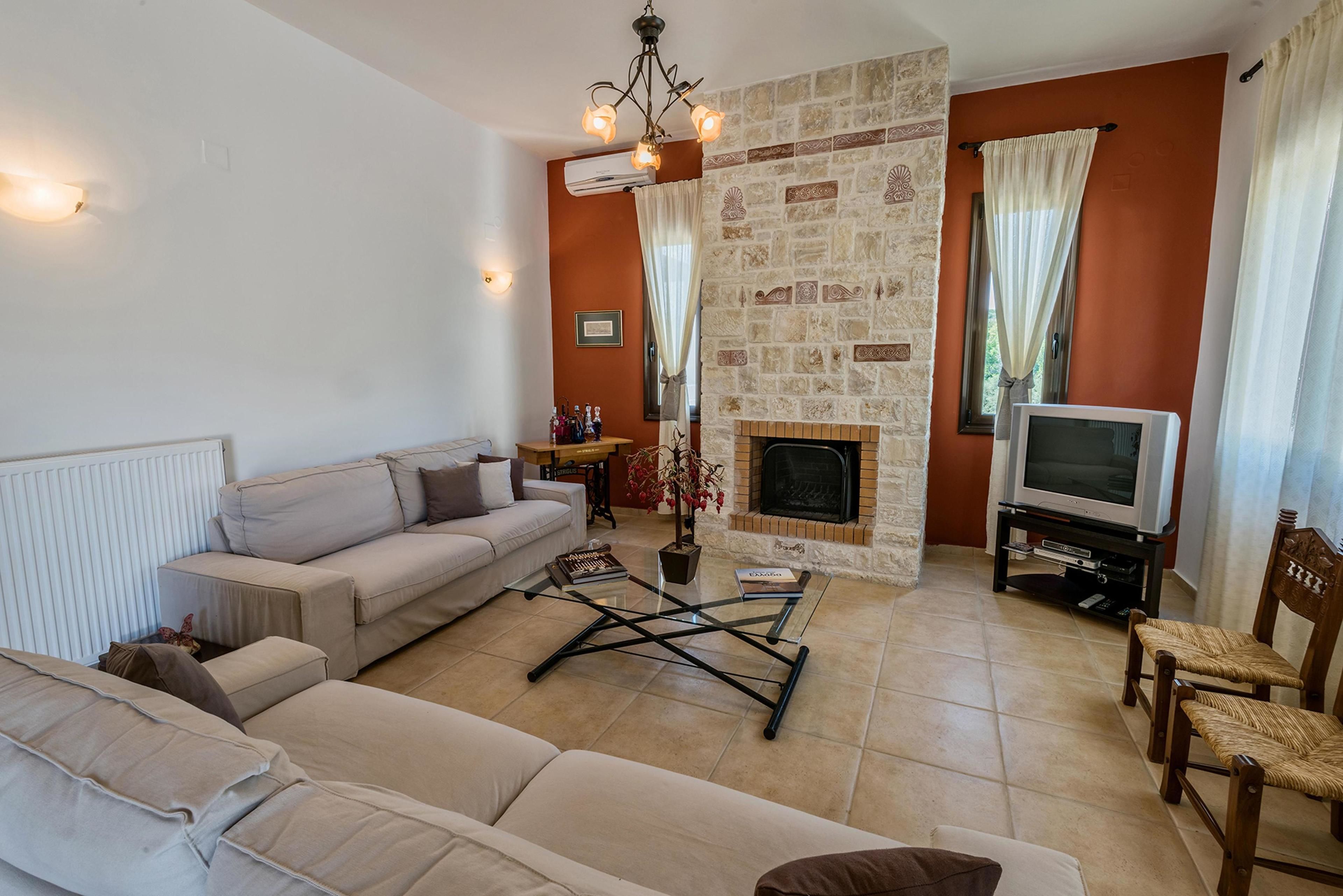 A living room with a beige sofa, a coffee table, a fireplace, a television, and a stone wall.