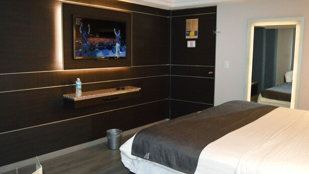 A hotel room with a large bed, a mounted TV, a small shelf, a trash can, and a door with a mirror. - Hotel Seoul - In Mexico City (Mexico City)
