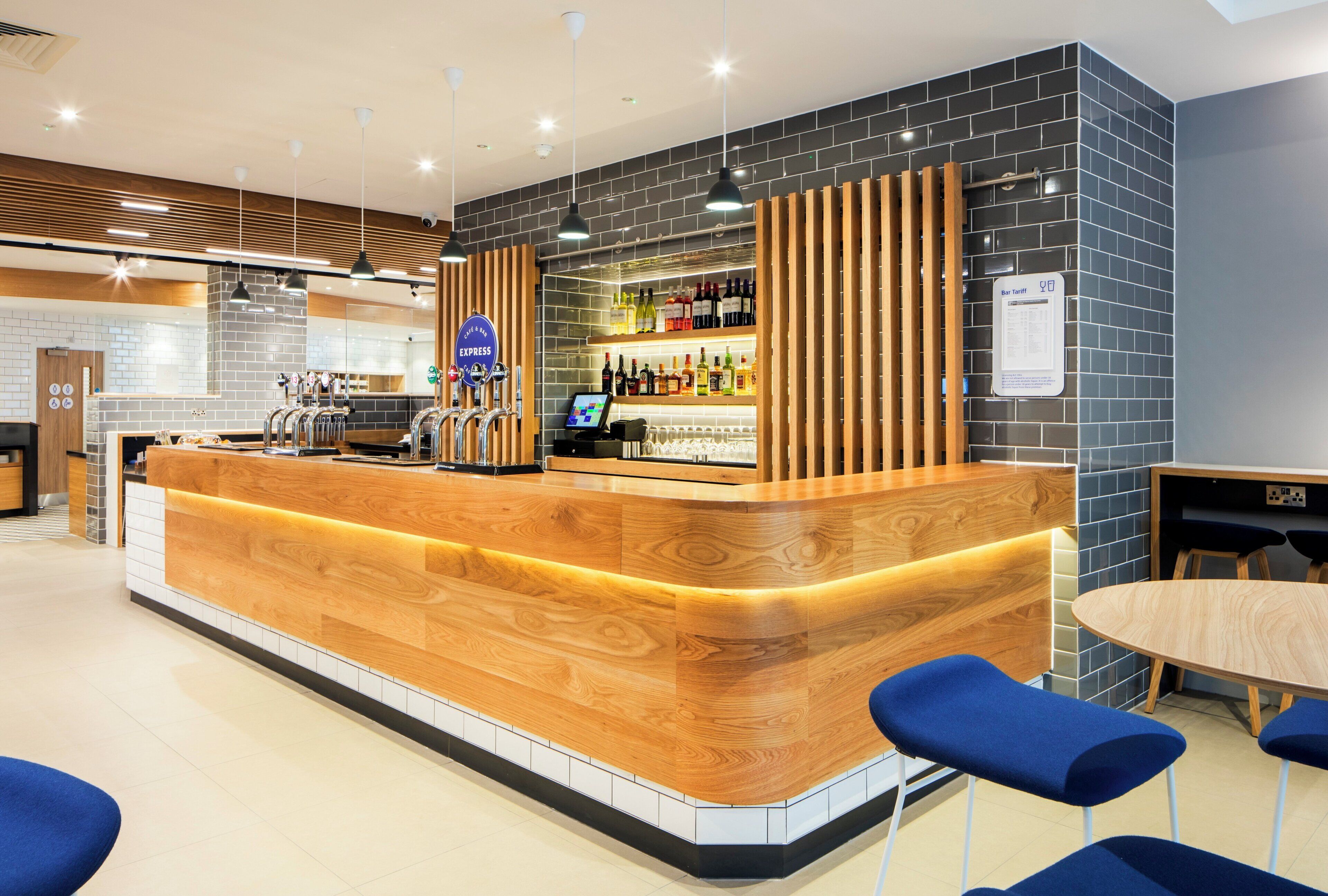 Zona de bar con mostrador de madera, taburetes y una variedad de botellas.