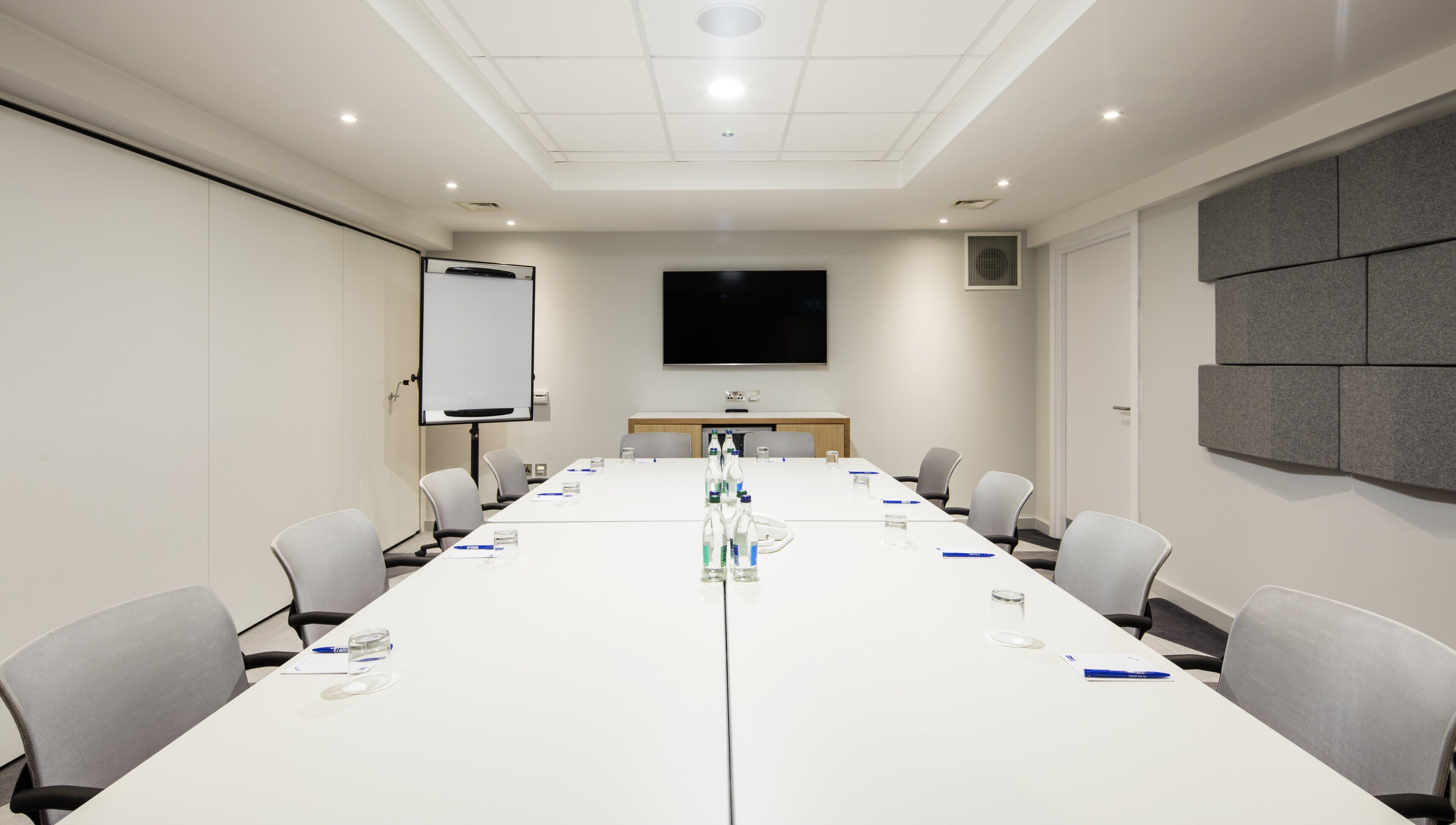 A conference room with a long table, chairs, a whiteboard, and a flat-screen TV.