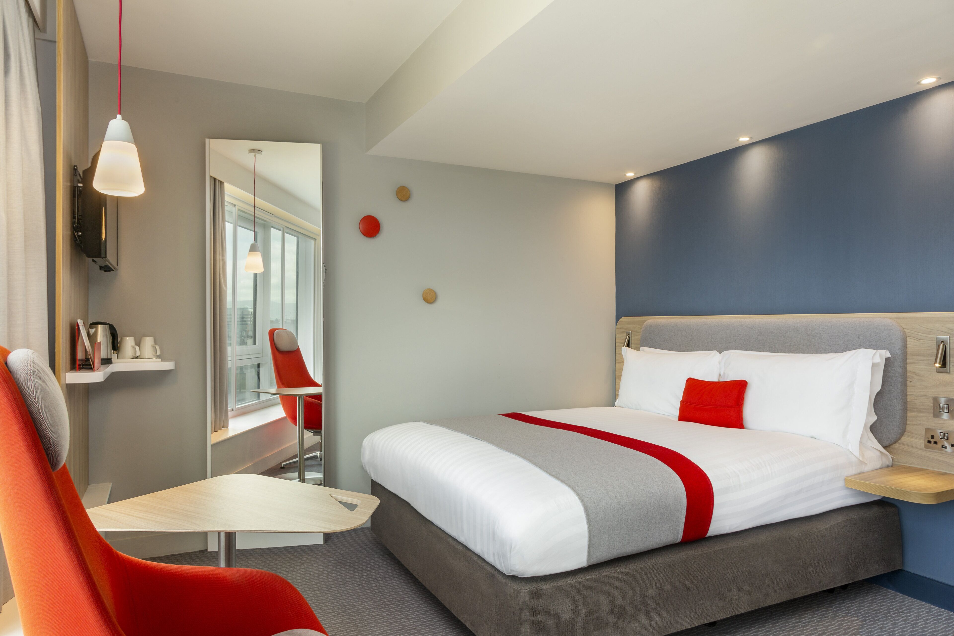 A modern hotel room with a bed, a desk, and a chair.