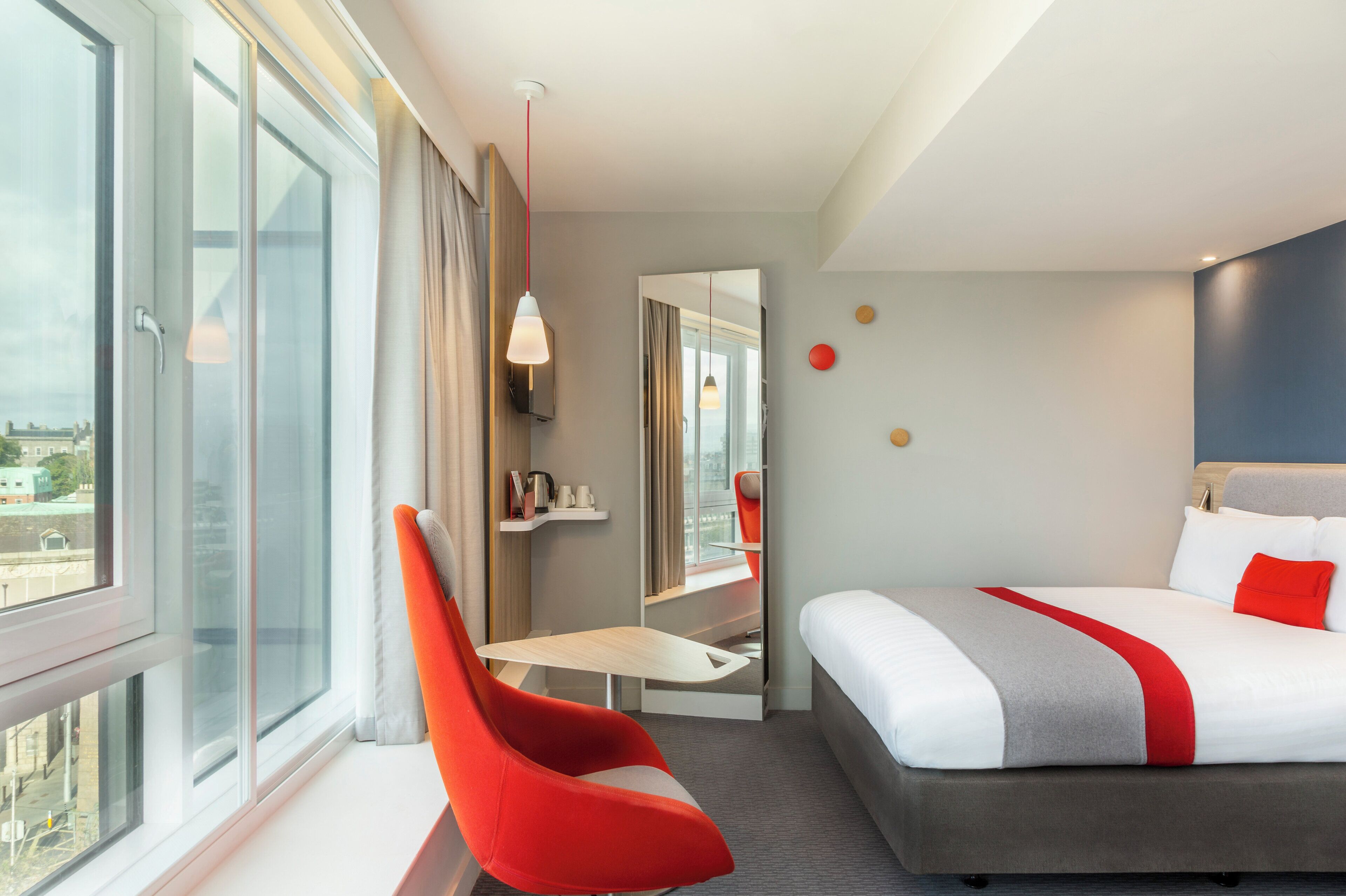 A hotel room with a bed, a desk, a chair, a window, and a view of the city.