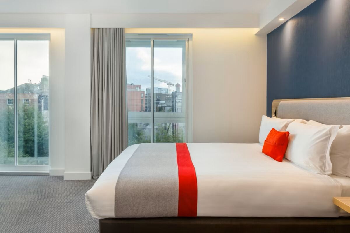 A hotel room with a large bed, a view of the city, and a window with curtains.