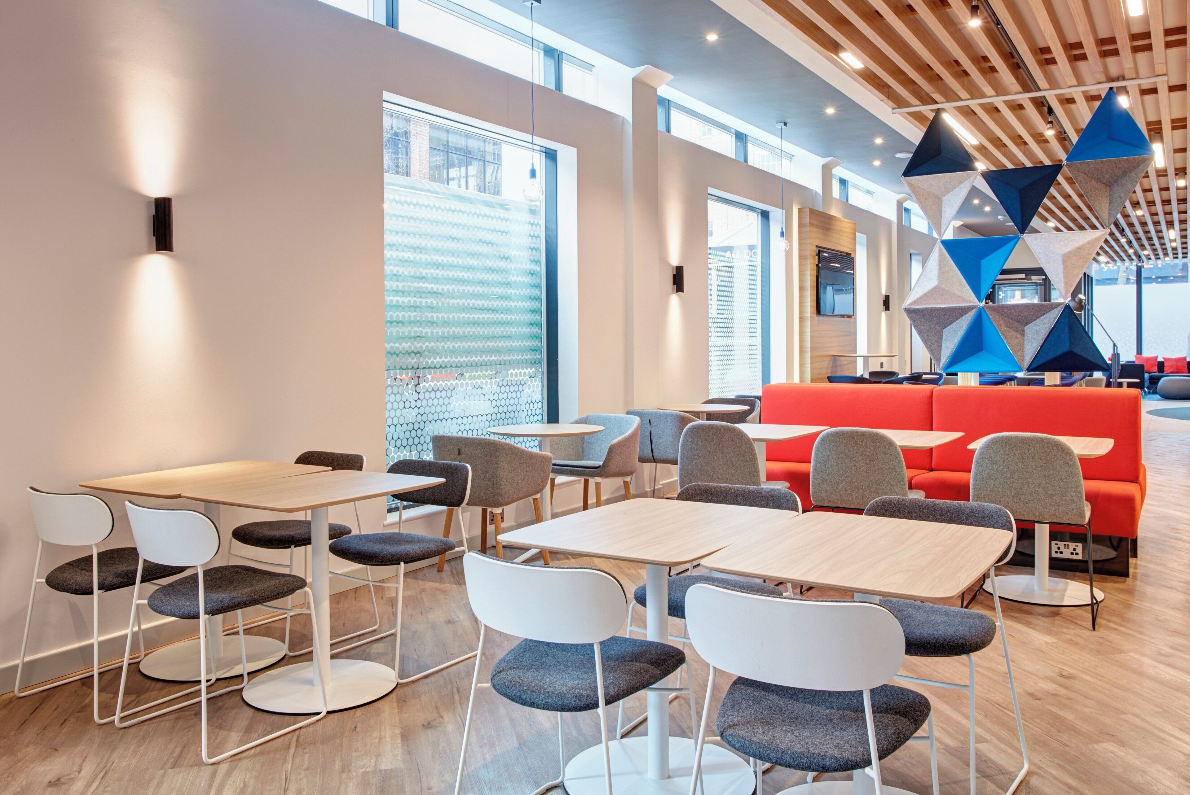Un espace repas moderne avec des tables et des chaises, un coin salon rouge et une grande fenêtre offrant une vue dégagée.
