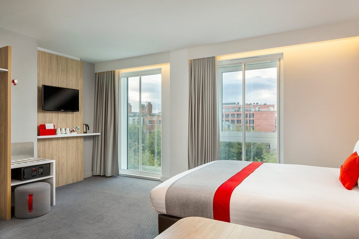 Une chambre d’hôtel équipée d’un lit, d’une télévision, d’une machine à café et d’une fenêtre donnant sur la ville.