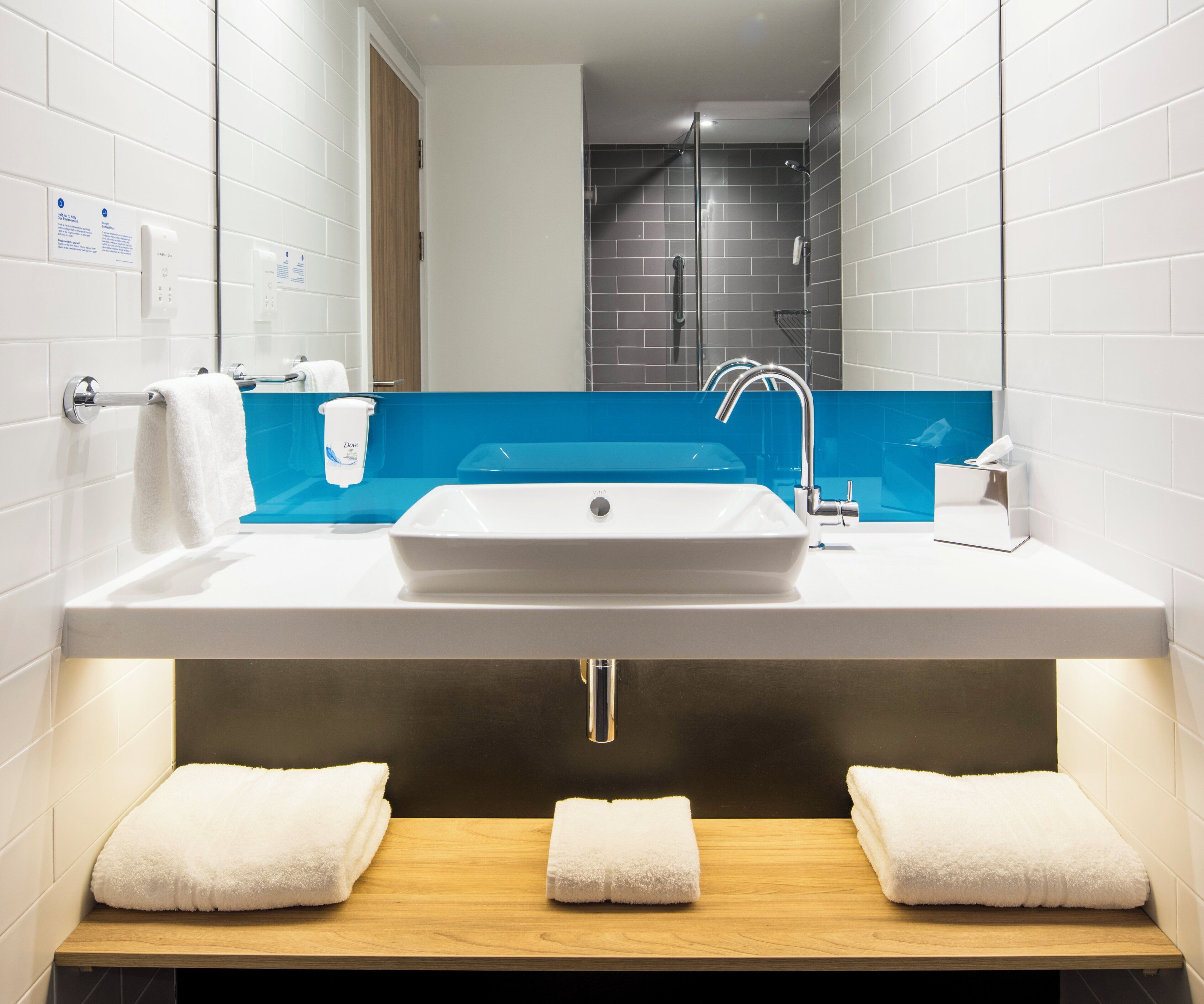A bathroom with a white sink, blue backsplash, and two towels on a wooden shelf.