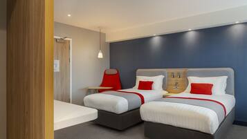 A modern hotel room with two beds, a wooden door, a small table, and a red lamp.