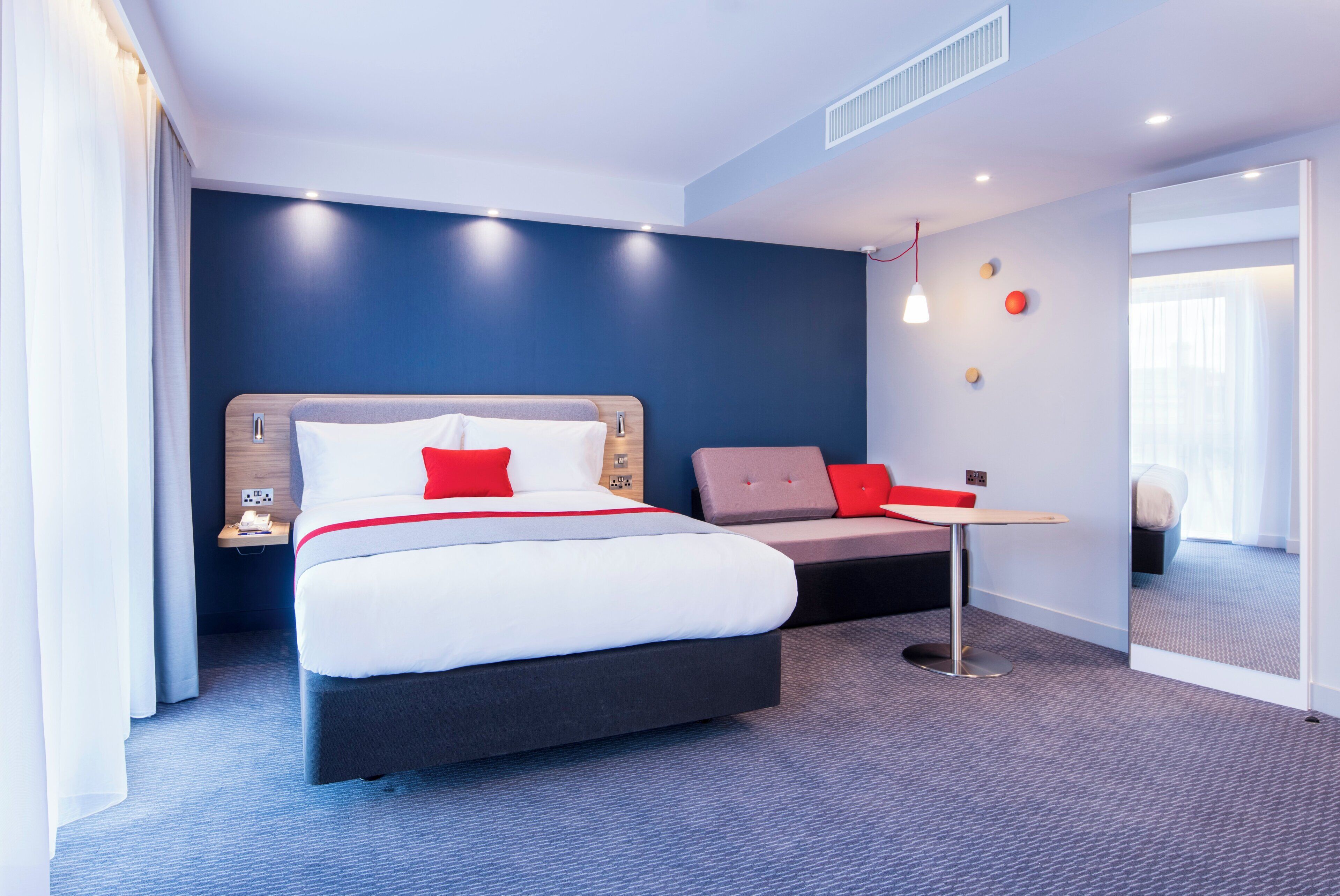 A modern hotel room with a large bed, a desk, and a seating area.
