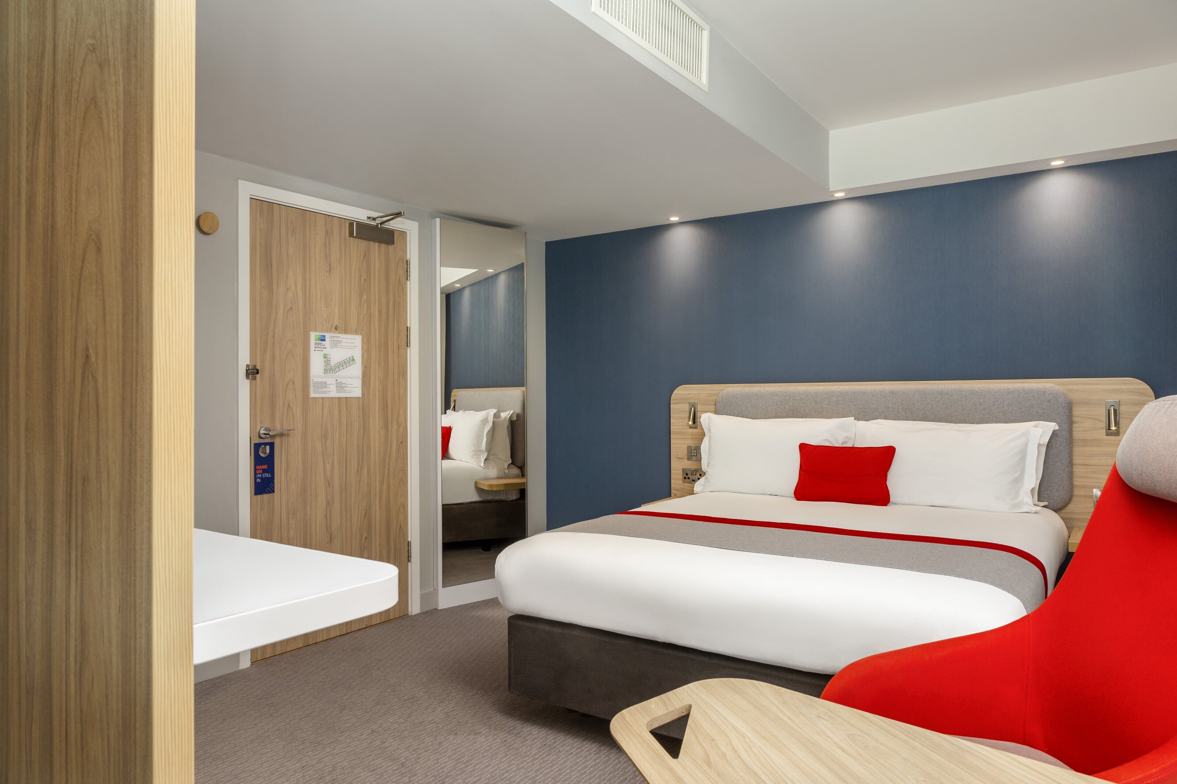 A modern hotel room with a large bed, a wooden door, and a small desk.