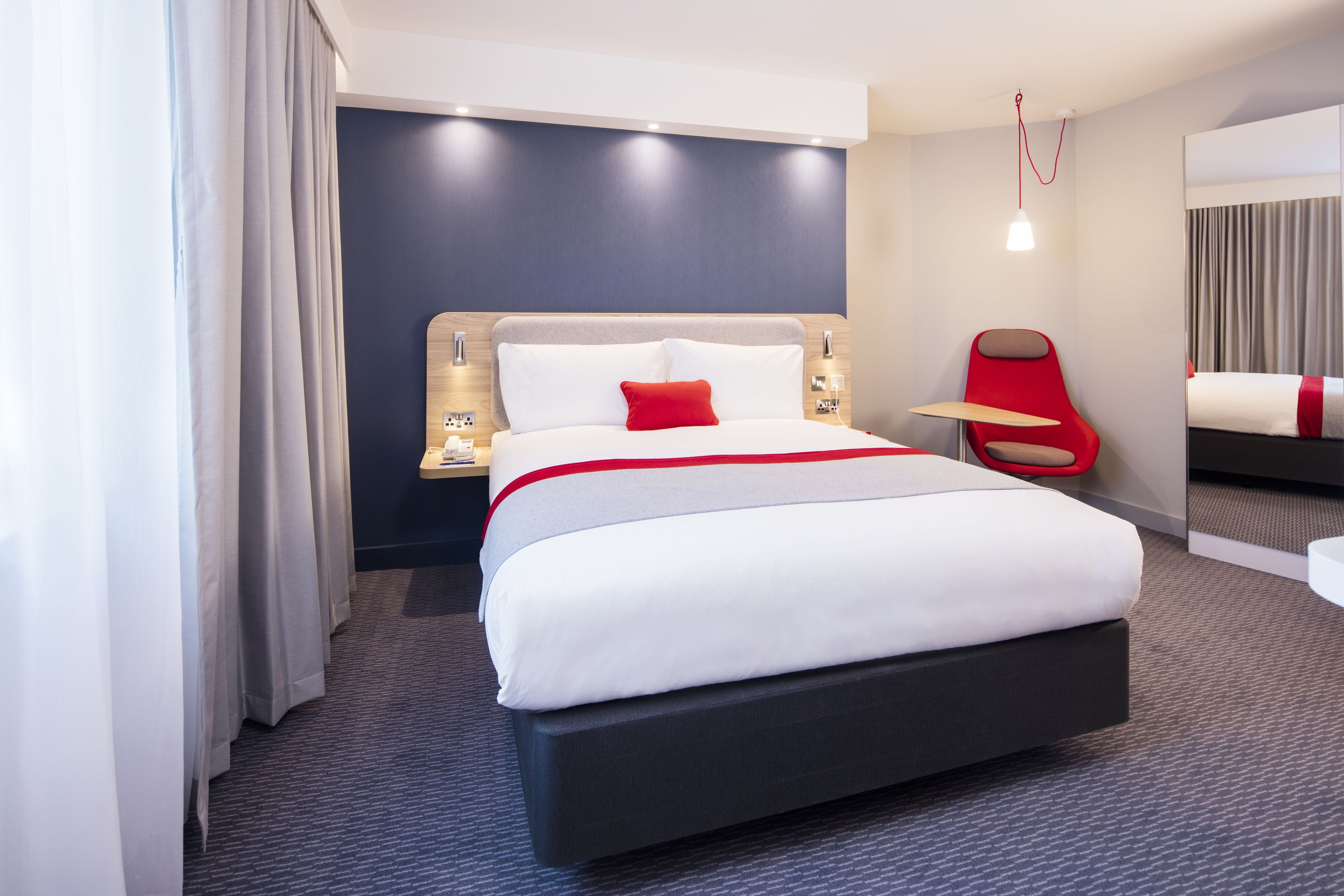A modern hotel room with a large bed, a red chair, and a small table.