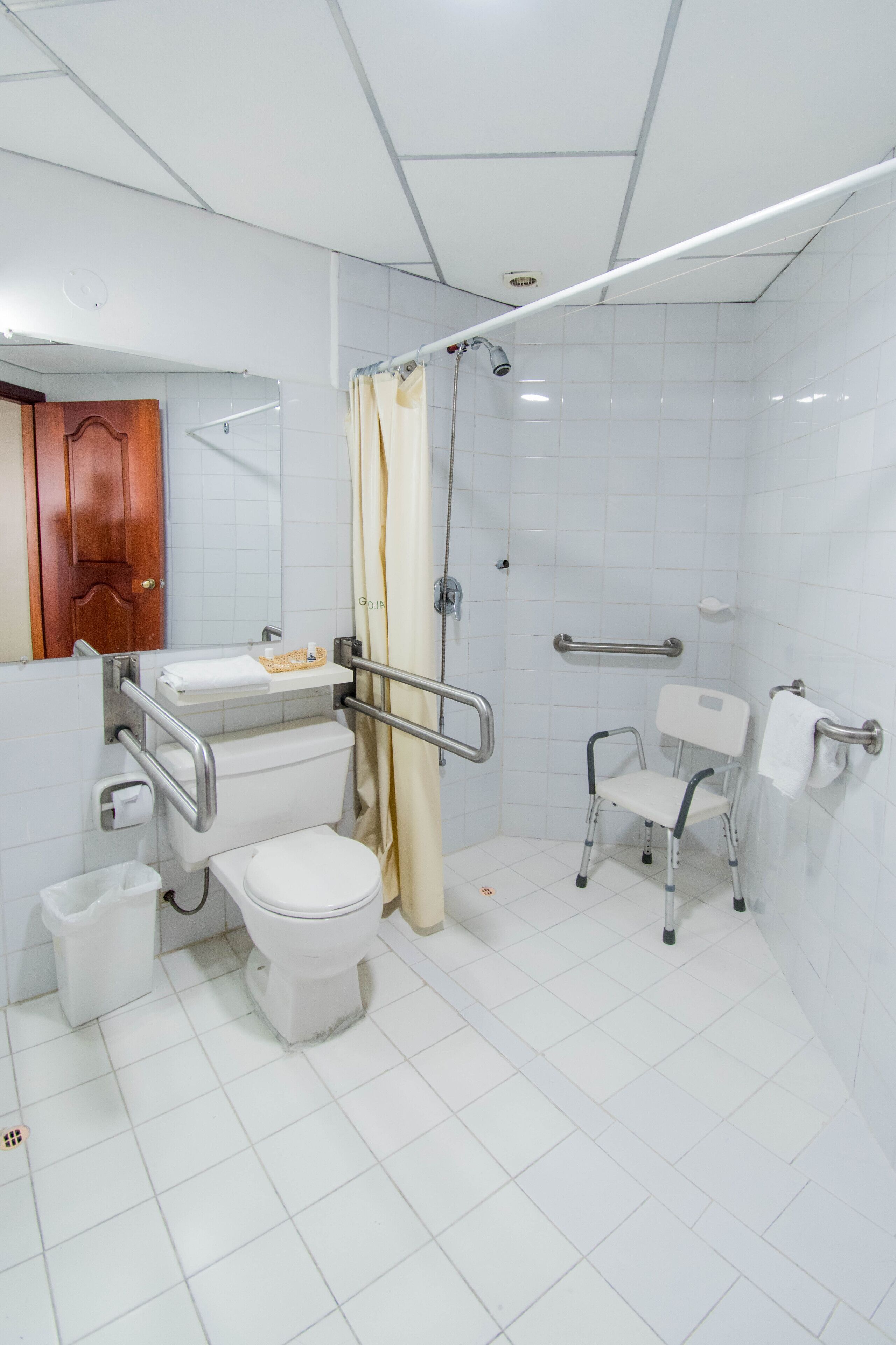 A bathroom with a toilet, bidet, and shower area, equipped with grab bars and a wheelchair-accessible chair.
