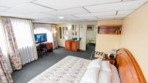 Ein Hotelzimmer mit einem großen Bett, einem Schreibtisch mit Computer, einem Kleiderschrank und einem Fernseher.