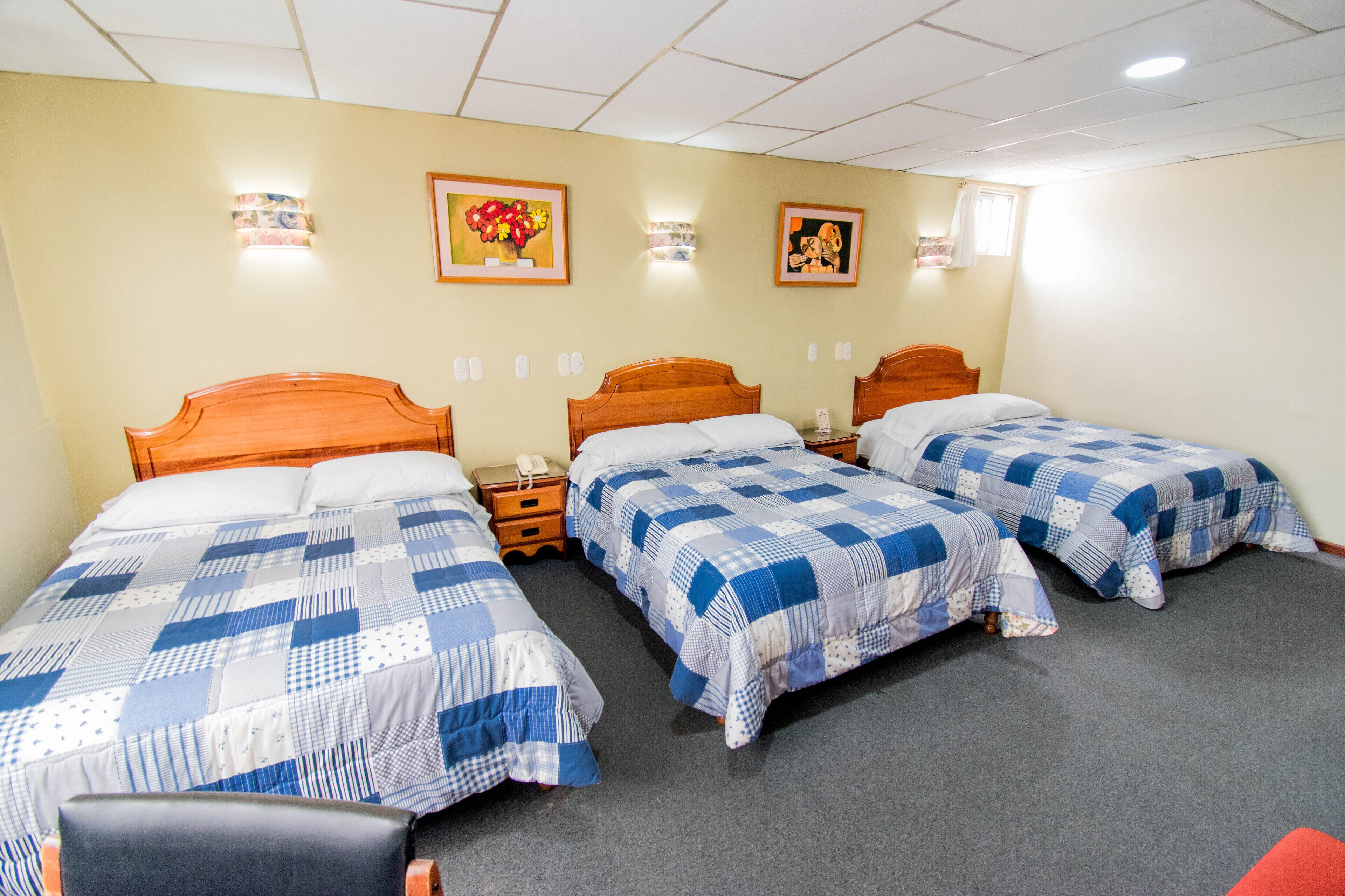 A hotel room with three single beds, a wooden headboard, a small desk with a telephone, and a chair.