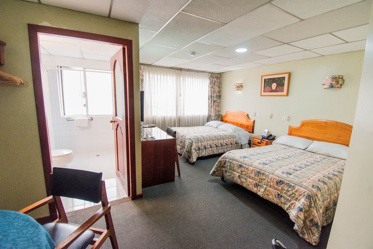 Habitación de hotel con dos camas, un escritorio, una silla, un baño y una puerta.