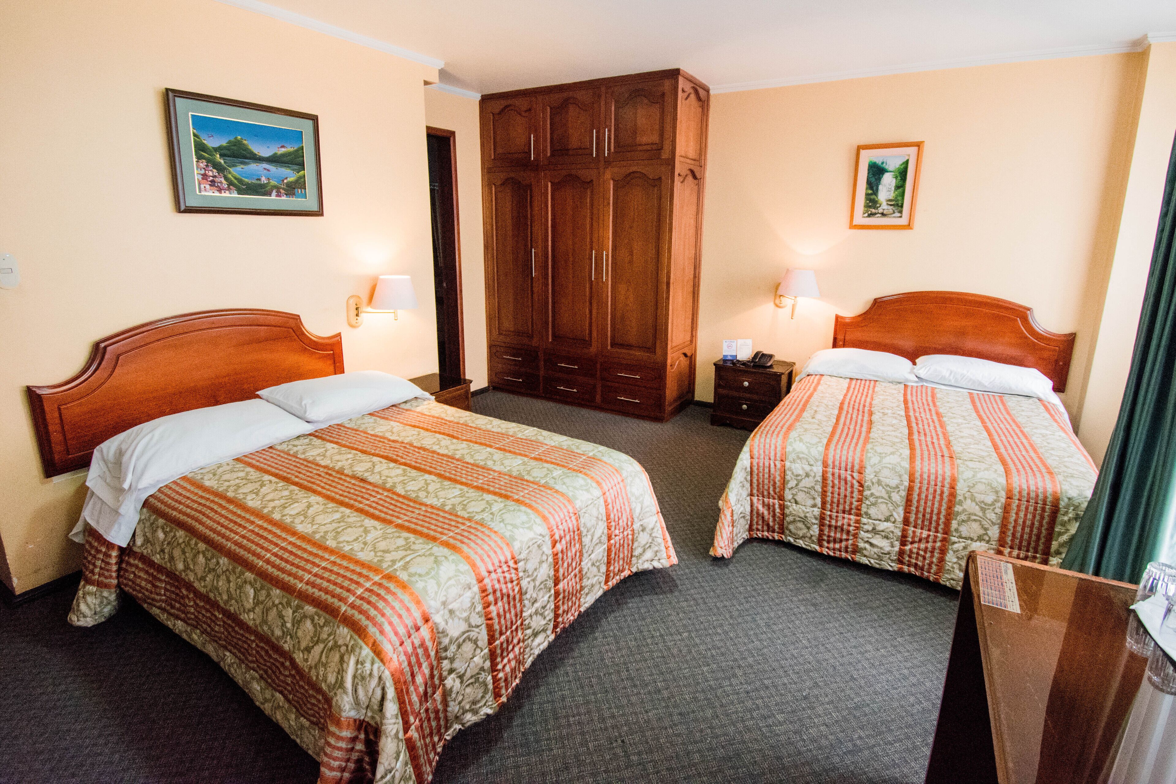 Habitación de hotel con dos camas, un armario y dos lámparas fijadas a la pared.