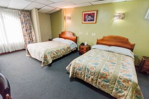 Habitación de hotel con dos camas, cabecero de madera, mesita de noche y lámpara de pared.