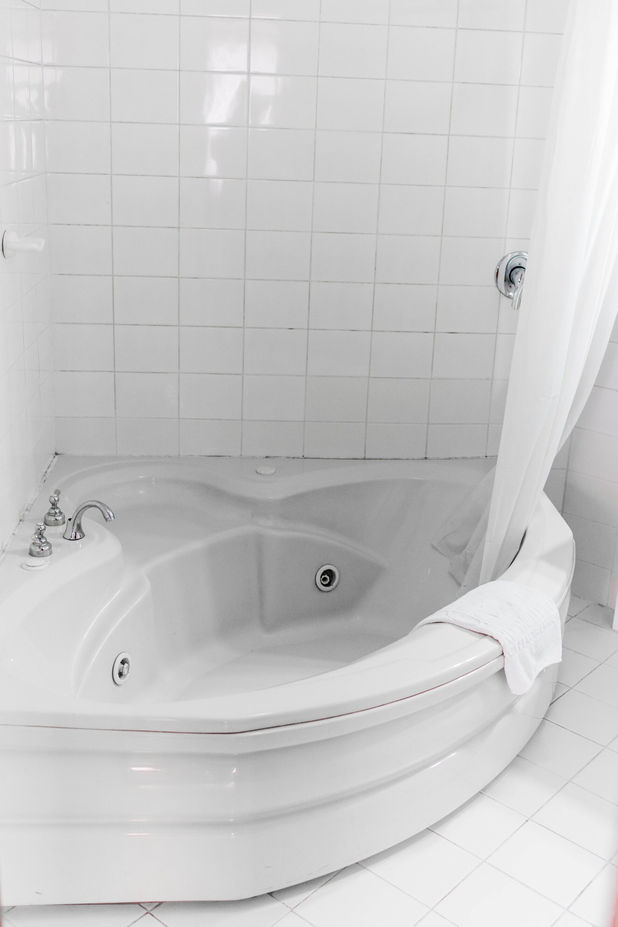 A corner bathtub with a shower curtain, a faucet, and a drain.