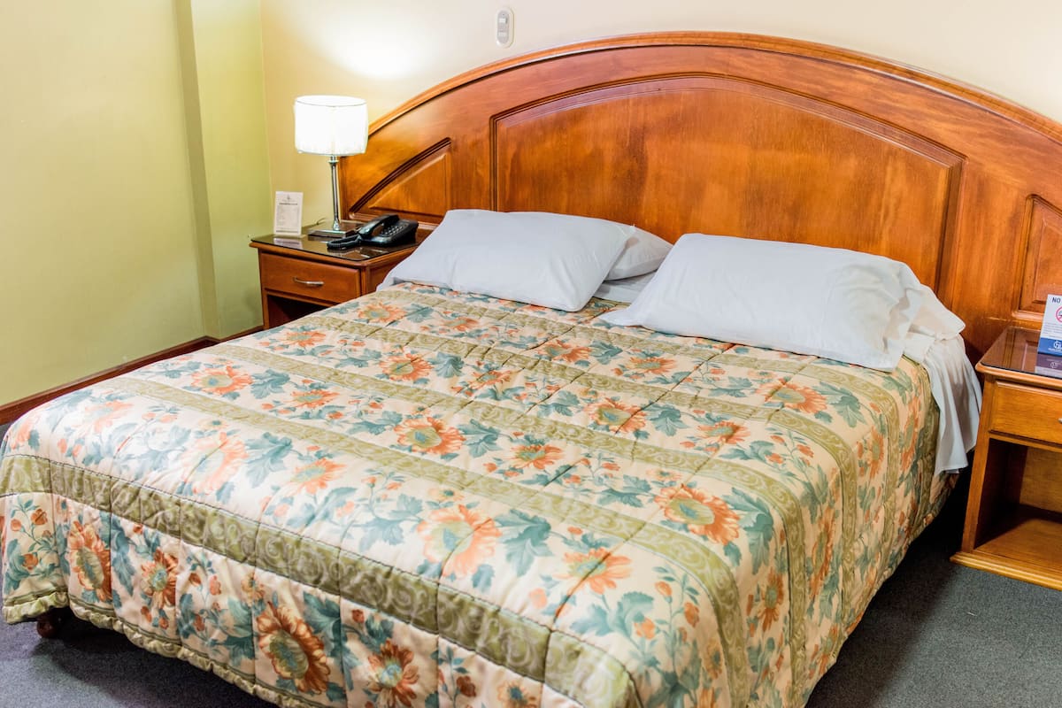 Una habitación de hotel con cabecera de madera, colcha estampada y mesita de noche con lámpara y teléfono.