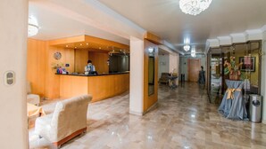 Eine Hotelhalle mit Rezeption, einer Sitzecke mit Sessel und einer Kandelaber.