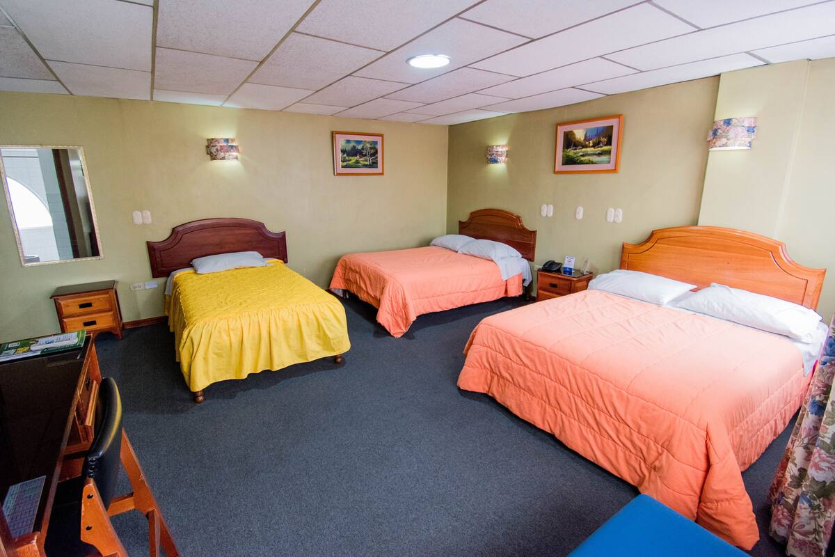 Una habitación de hotel con tres camas individuales, un escritorio con silla y una mesita.