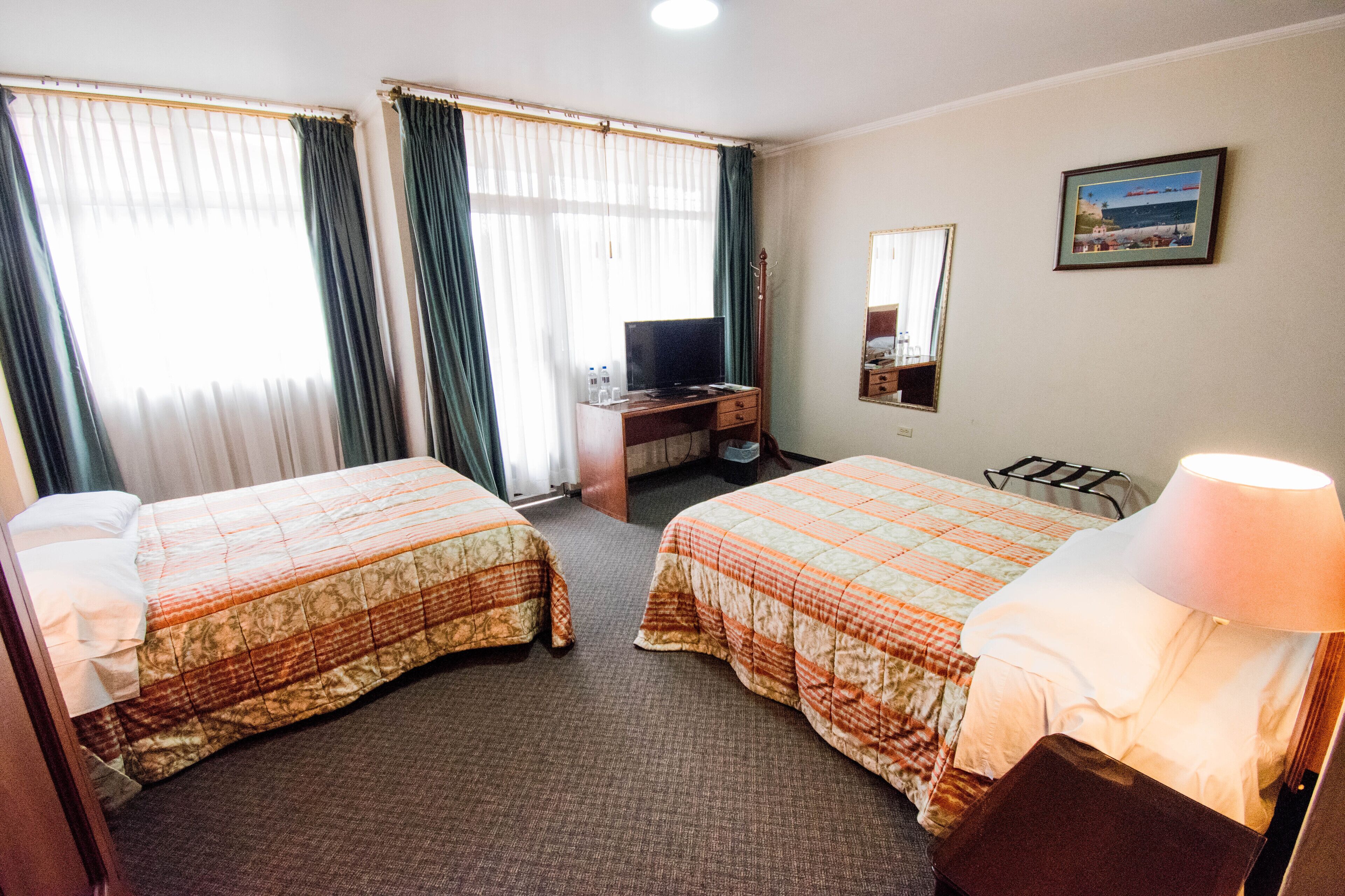 A hotel room with two beds, a desk with a computer, a lamp, and a painting on the wall.