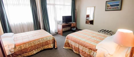 Habitación de hotel con dos camas, un escritorio con computadora, una lámpara y un cuadro en la pared.