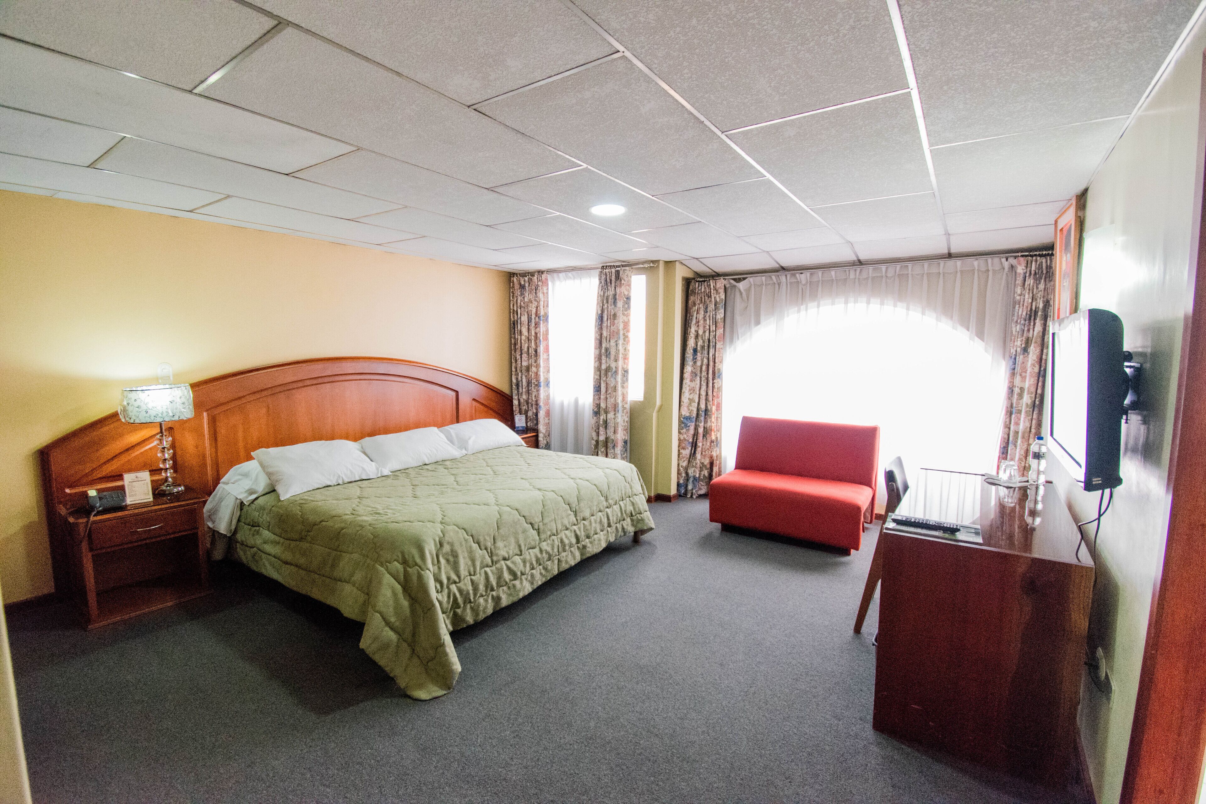 Quarto de hotel com uma cama, mesa de cabeceira, escrivaninha, cadeira e televisão.